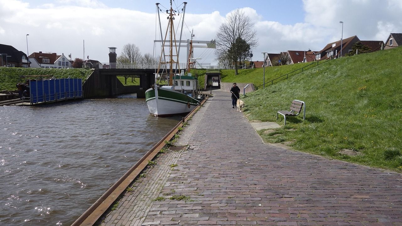 Der Weg an der Harle in Carolinensiel, mit Schiffen am Anleger und dem Deich daneben.