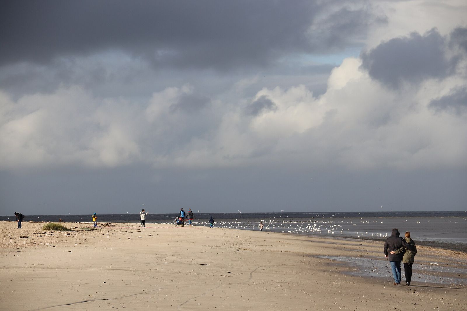 Der weite Sandstrand von Schillig mit Spaziergängern am Wasser.